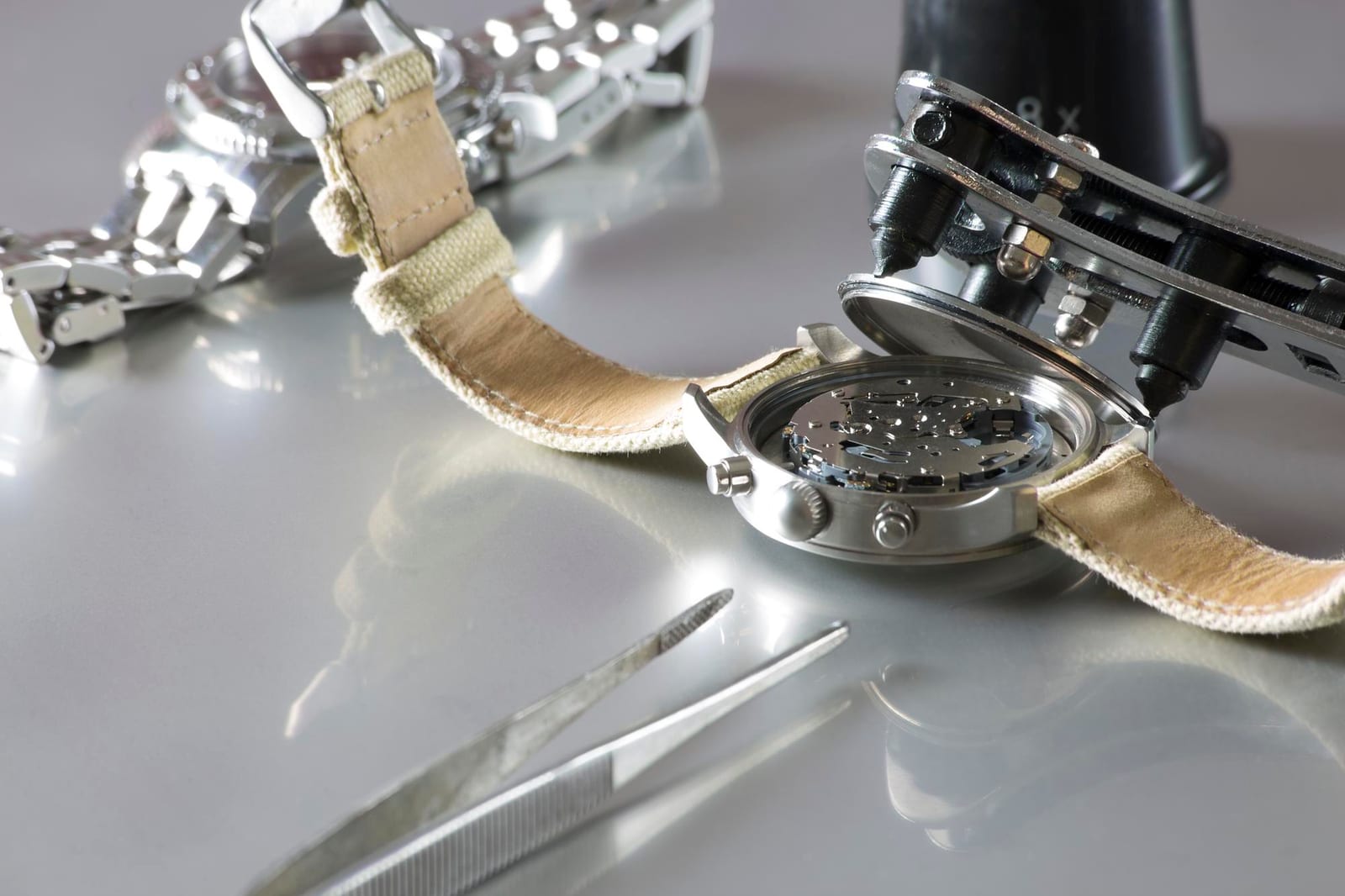 Movimento di un orologio aperto sotto una lente d'ingrandimento, con cacciaviti di precisione a lato