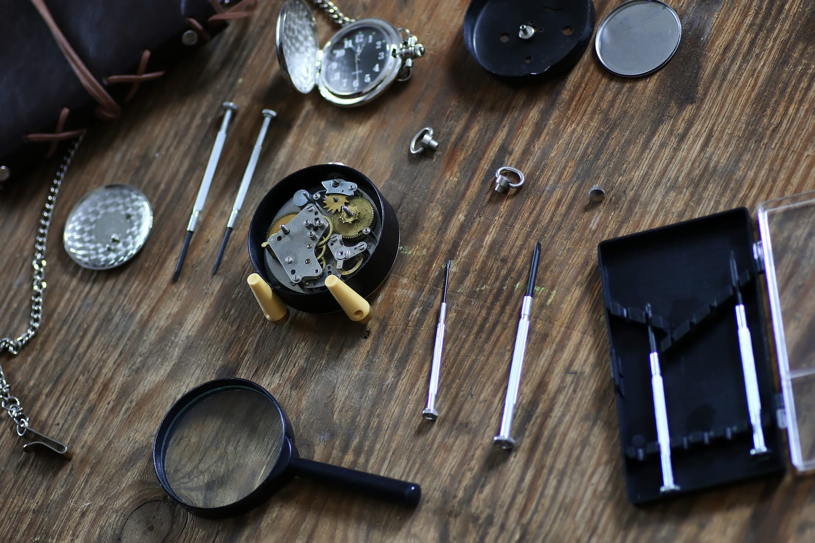 Banco da lavoro orologiaio con un orologio da tasca aperto, lente d'ingrandimento e cacciaviti in ordine